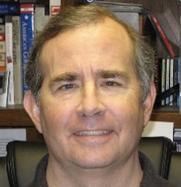 Photo of a middle-aged white man with brown hair standing in front of bookshelves.