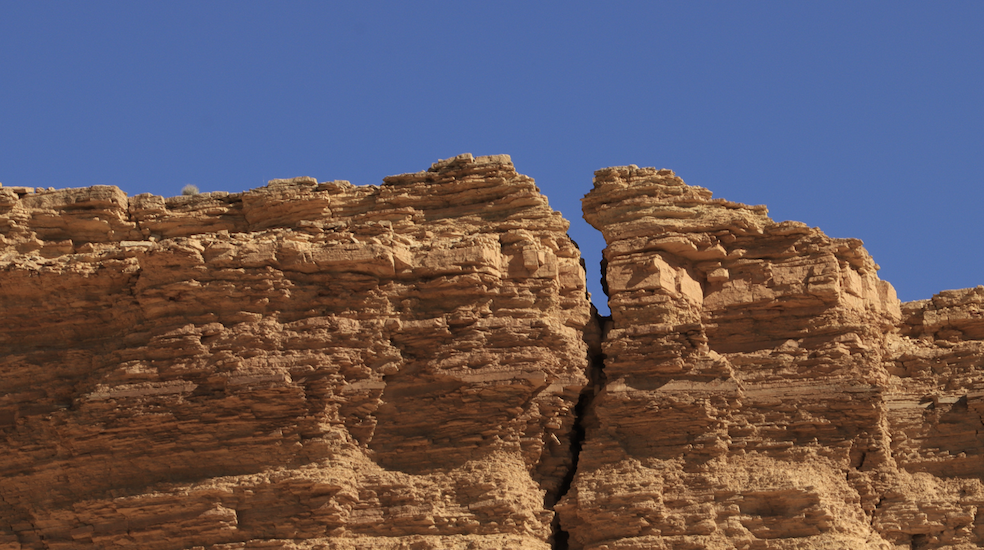A photo of a big vertical crack in a rock cliff underneath a bright blue sky.