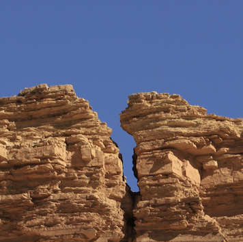 A photo of a big vertical crack in a rock cliff underneath a bright blue sky.